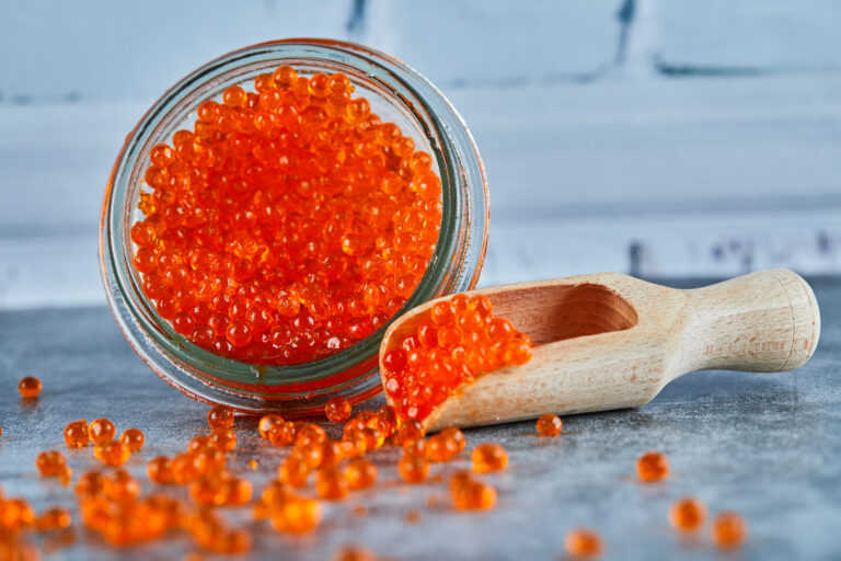 A jar of red caviar and wooden spoon on marble background