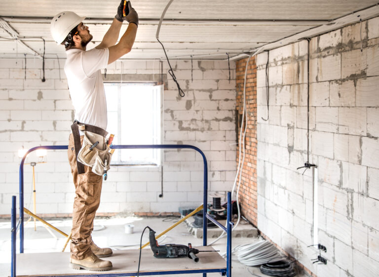 Electrician installer with a tool in his hands, working with cable on the construction site.
