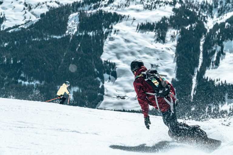Closeup of a person snowboarding and a skier skiing on a snowy mountain during daylight