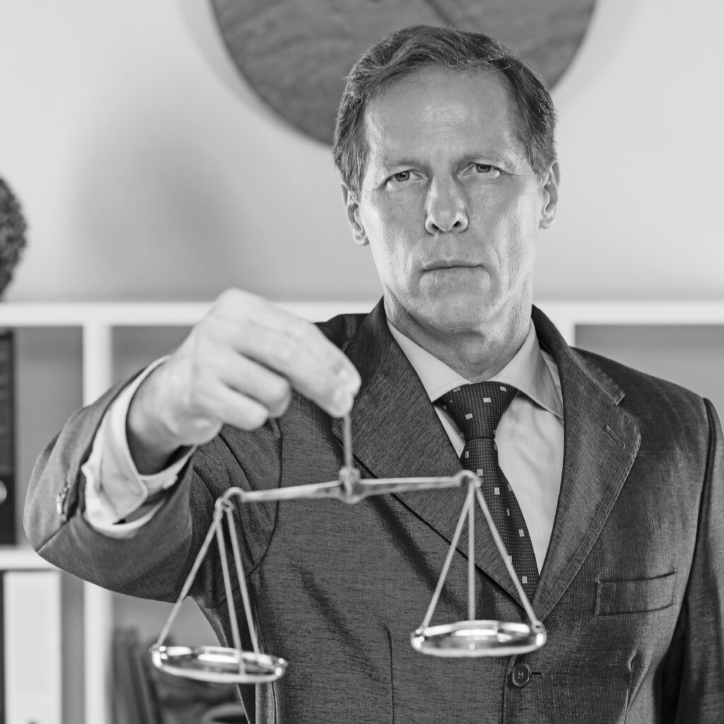 golden justice scale behind the lawyer signing the document on desk